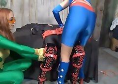 Two costumed dominatrices bind and restrain a helpless man in a dim industrial chamber