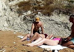 Gals sunbathing on the beach, they watch 2 dude and invite 'em to share their bluncket