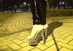 crossdresser walks on the street in transparent high heels and latex leggings